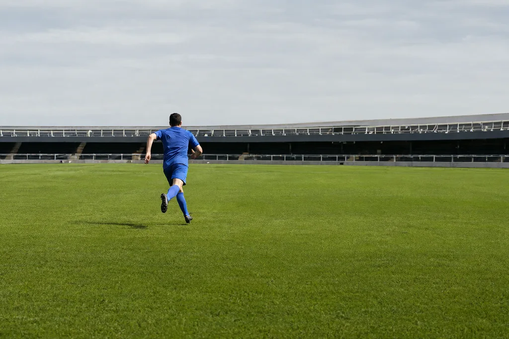 Player sprinting across the middle of a green pitch seen from the far touchline